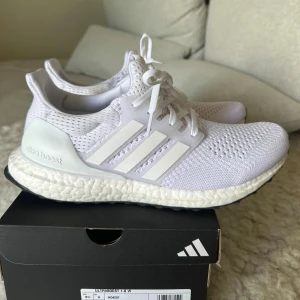 Vita Adidas Ultraboost 1.0 sneakers - Fräscha Adidas Ultraboost 1.0 sneakers i helvitt med klassiska tre ränder på sidan. Ovandel i ventilerande mesh och sula med Boost-dämpning för maxad komfort. Perfekta för både träning och streetstyle. Snygg, sportig look med snörning och svart yttersula. Nypris 2300kr mitt pris 1400kr!! Skorna har knappt används. 