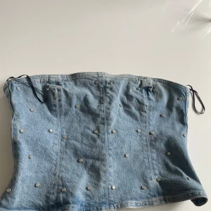 Ljusblå jeanskorsett med diamant nitar - Säljer en snygg ljusblå jeanskorsett med silvriga nitar över hela toppen. Toppen är axelbandslös och har dragkedja bak för enkel på- och avtagning. Aldrig använd