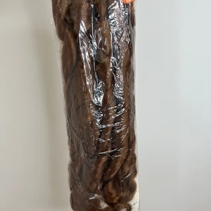 Princess French Curl Brunt lockigt  - Säljer ett paket med långt, lockigt syntethår i en varm brun nyans. Perfekt för att skapa volym och längd till din frisyr. Håret är förpackat i plast och har en naturlig glans. Märket syns delvis på förpackningen men är otydligt.