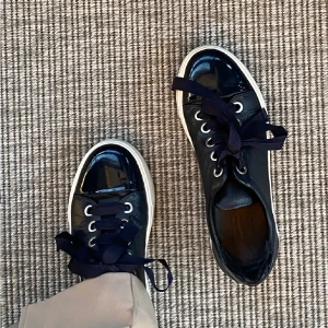 Mörkblåa sneakers - Snygga BLÅA sneakers med glansiga lackdetaljer på tån och breda svarta snören. Skorna har en vit, tjock sula och silverfärgade öljetter. Perfekta för en trendig och stilren look. Köpa på Vinted men passade inte! Lånade bilder, skriv för egna💗