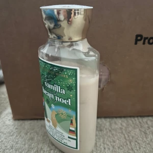 Body lotion Vanilla Bean Noel från Bath & Body Works - Body lotion med doft av vanilj från Bath & Body Works. Flaskan har guldigt lock och grön etikett med juligt motiv. Innehållet är ljusbeige och flaskan rymmer 236 ml.