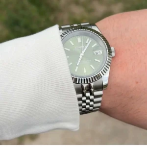 Seiko mod datejust green dial - Säljer en Seiko herrklocka med automatisk urverk, grön urtavla och datumvisning. Klockan har en silverfärgad boett och länkarmband i rostfritt stål. Klassisk räfflad bezel och transparent baksida som visar urverket. Perfekt accessoar för dig som gillar stilrena detaljer.
