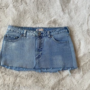 Blå jeanskjol från Faded Glory - Snygg blå jeanskjol från Faded Glory med stretch. Kjolen har klassisk femficksdesign, rå kant nertill och dekorativa sömmar på bakfickorna. Perfekt för dig som gillar en avslappnad och trendig stil. Står ingen storlek men passar S