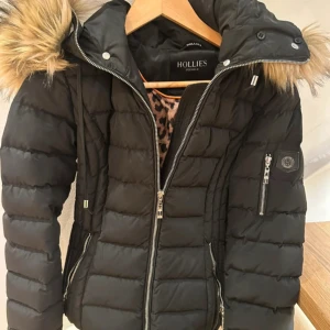 Hollies jacka  - Äkta Hollies jacka i storlek 34, köpt för ett par år sedan men i fink skick då den används sparsamt. Figursydd modell. Stor luva med avtagbar päls. Det är fakepäls. Nypris runt 4000-5000 kr. Skriv vid frågor eller funderingar!😊