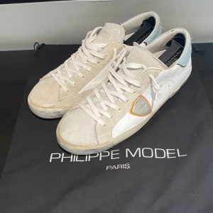 Philippe model skor - Säljer nu mina vit, orange, blåa Philippe model skor. Säljer skorna då dom inte passar mig längre, skorna är i helt okej skick. Lite skador på hälen som man kan se på sista bilden och där fram på skorna är mockan lite sliten och smutsig. Annars riktigt feta skor till sommaren!