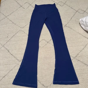 Mörkblå utsvängda leggings från Lululemon - Säljer ett par blå leggings från Lululemon med bootcut-ben. De har hög midja och är tillverkade i ett stretchigt syntetmaterial som passar perfekt för träning eller en avslappnad stil. De är svåra att få fram färgen på men sista bilden visar nog bäst, mörkblåa. US 6/S, align flared. Endast använda en gång