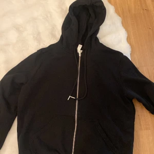 Svart hoodie med dragkedja - Säljer en svart hoodie med dragkedja framtill och huva. Tröjan har långa ärmar och två fickor framtill. Perfekt för en avslappnad stil och enkel att matcha med det mesta. Knappt använd.