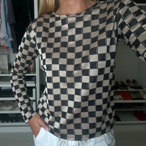 Beige och svart långärmad tröja från Fendi - Säljer en snygg långärmad tröja från Fendi i beige och svart med schackrutigt mönster och diskret Fendi-logga i rutorna. Tröjan har rund halsringning och är i ett mjukt, stretchigt material. Perfekt för dig som gillar statement-plagg!