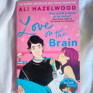 Love on the Brain - En romantisk roman av Ali Hazelwood med färgstarkt tecknat omslag i rosa och blått. Boken handlar om Bee Königswasser och hennes äventyr inom vetenskap och kärlek. Perfekt för dig som gillar smart och rolig feelgood.