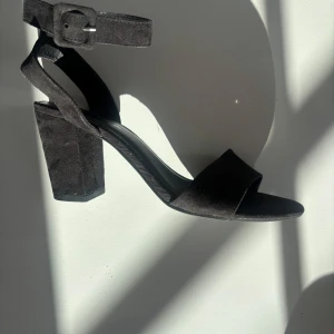 Svarta klackskor med ankelrem - Svarta sandaler från DS Shoes med bred klack och öppen tå. Skorna har en bred rem över tårna och justerbar ankelrem med spänne. Mycket bra skick 