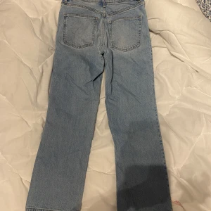 Ljusblå raka jeans - Säljer ett par ljusblå jeans med raka ben och klassisk femficksdesign. Jeansen har medium midja och stängs med knappar framtill. Perfekta för en avslappnad och stilren look. 