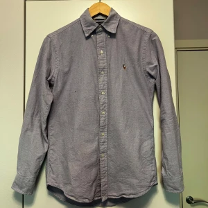Ljuslila skjorta från Polo Ralph Lauren - Säljer en klassisk ljuslila skjorta från Polo Ralph Lauren i modellen Classic Fit. Skjortan har knappar framtill, lång ärm och en liten broderad logga på bröstet. Perfekt för dig som gillar stilrena plagg med diskreta detaljer.