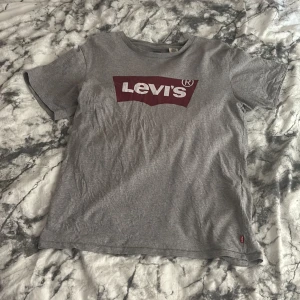 Grå t-shirt från Levi's - Grå t-shirt från Levi's med klassisk röd logga framtill. T-shirten har rund halsringning och korta ärmar. Tillverkad i mjuk bomull, perfekt för en avslappnad stil.