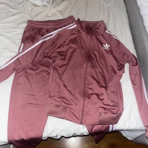 Rosa Adidas träningsset med dragkedja - Säljer ett rosa Adidas träningsset med vit logga och vita ränder längs ärmar och ben. Jackan har dragkedja. Perfekt för träning eller chill. Det säljs för sig men också tillsammans!  Snygg och sportig look! I storlek S HELT NY!