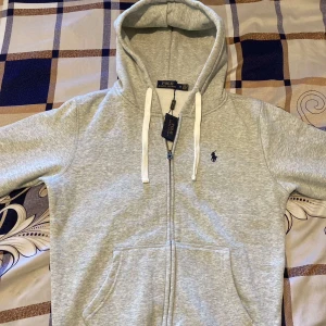  Polo Ralph Lauren hoodie (grå) - Hej säljer denna helt nya ljusgrå hoodie från Polo Ralph Lauren med dragkedja, två framfickor och den klassiska broderade loggan på bröstet. Mjuk, lätt och stilren – perfekt för svala sommarkvällar eller en avslappnad vardagslook året runt. M passar även S hör av er vid frågor 