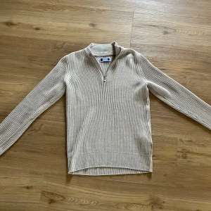 Beige ribbad tröja med dragkedja från Jack & Jones - Säljer en beige ribbad tröja från Jack & Jones med halv dragkedja vid halsen. Tröjan har lång ärm och är tillverkad i ett mjukt material, tröjan är aldrig använd, endast testad😃