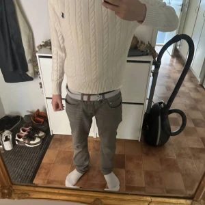 Vit kabelstickad tröja från Polo Ralph Lauren - Säljer en klassisk vit kabelstickad tröja från Polo Ralph Lauren med broderad logga på bröstet. Tröjan har lång ärm och ribbade muddar vid ärmslut och nederkant. Perfekt för en stilren och tidlös look.