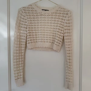 Beige stickad croppad tröja från Gina Tricot - Säljer en beige stickad croppad tröja från Gina Tricot med lång ärm och öppen rygg. Tröjan har ett luftigt, hålmönstrat stickat material och ribbade muddar vid ärmslut och nederkant. Perfekt för lager-på-lager-stil!
