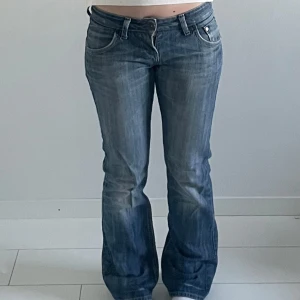 Blå bootcut jeans från Cross Jeans - Säljer ett par blå bootcut jeans från Cross Jeans med låg midja. Jeansen har klassiska fem fickor, lätt slitna detaljer och stängs med dragkedja och knapp. Perfekta för dig som gillar en avslappnad och tidlös stil.