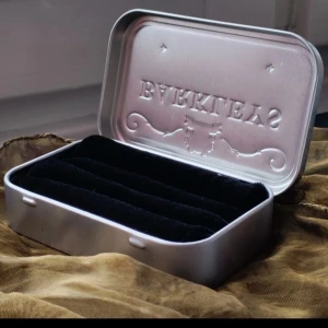 Litet smyckestillverkning  - Ett litet och smidigt smyckeskrin. Får enkelt plats i fickan eller väskan! Gjort av mig. Ringar på bilden ingår ej.  Mått: 9,5x5,5x2,0 cm Material: Gjort av en tablettask i metall och återvunna textilier. 100% återbruk