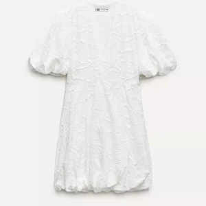 Vit kortklänning med puffärm från Zara - Superfin vit kortklänning från Zara med v-ringning och puffiga kortärmar. Klänningen har ett subtilt blommigt mönster i tyget och en lätt volang nertill. Perfekt för sommarens alla tillfällen!