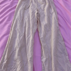 Beige linnebyxor med dragsko - Säljer ett par beige linnebyxor från Åhléns i storlek S. Byxorna har breda ben och dragsko i midjan för en bekväm passform. Perfekta för varma dagar och en avslappnad stil.