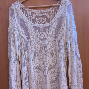 Vit spetsblus med blommigt mönster - Säljer en romantisk vit blus i spets med vackert blommigt broderi. Blusen har lång ärm och är transparent med fina detaljer över hela plagget. Perfekt för dig som gillar bohemisk stil och vill ha något unikt i garderoben.