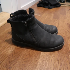 Svarta boots med dragkedja - Svarta boots med rund tå och dragkedja på sidan. Skorna har en platt sula och är fodrade på insidan för extra värme. Perfekta för kyligare dagar och har en enkel, stilren design.