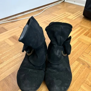 Svarta boots med spänne - Svarta boots i mocka med rund tå och dekorativt spänne på sidan. Skorna har platt sula och är perfekta för dig som gillar en stilren look med lite extra detalj. Passar bra till både jeans och kjol.