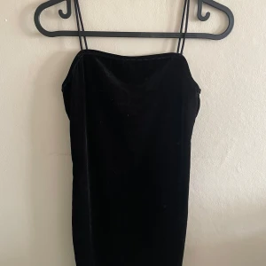 Svart sammetsklänning med smala axelband - Säljer en svart sammetsklänning med smala axelband och rak passform. Klänningen är enkel och elegant, perfekt för dig som gillar minimalistisk stil. Materialet är mjukt och har en fin lyster.