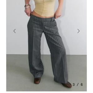 Grå low waist kostymbyxor med vita ränder från Monki - Snygga grå kostymbyxor från Monki med vita vertikala ränder. Byxorna har normal passform och vida ben, samt hällor för bälte och fickor bak. Tillverkade i återvunnen polyesterblandning. Står storlek 40, men är mer storlek 38. Aldrig använda