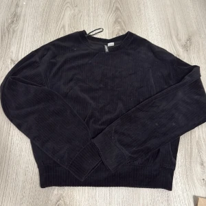 Svart manchestertröja från H&M Divided - Säljer en svart långärmad tröja från H&M Divided i mjuk manchester. Tröjan har rund halsringning och en relaxed passform, perfekt till många olika outfits. Enkel och stilren design.