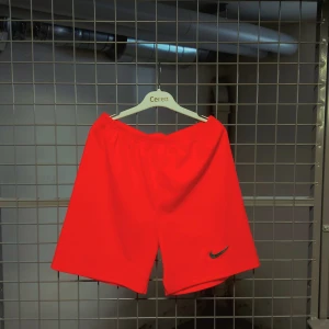 Röda träningsshorts från Nike - Säljer ett par röda träningsshorts från Nike med elastisk midja och klassisk Nike-logga på ena benet. Shortsen har en enkel design och är perfekta för sport eller gym. Materialet känns lätt och luftigt.