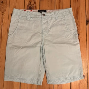 Turkosa shorts från Bondelid - Snygga turkosa shorts från Bondelid med klassisk design och normal passform. Shortsen har fickor fram och bak, bälteshällor och stängs med knapp och dragkedja. Perfekta för varma dagar och enkel att matcha med olika stilar. Storlek 32.