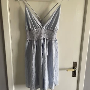 Ljusblå sommarklänning - Söt ljusblå klänning med smock i midjan och tunna, korsade axelband. Klänningen har v-ringning och är ärmlös, perfekt för t.ex midsommar💐Endast använd någon enstaka gång men helt som ny. Köparen står för frakt💗