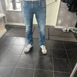 Blå Replay Anbass jeans - Säljer ett par blå Replay Anbass jeans med klassisk femficksdesign och lätt slitna detaljer. Jeansen har normal passform och raka ben, perfekt för en avslappnad stil. 