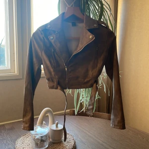 Brun croppad skinnjacka från SHEIN - Säljer en brun croppad skinnjacka från SHEIN med dragkedja och bälte i midjan. Jackan har långa ärmar och klassisk bikerkrage. Perfekt för dig som vill ha en edgy look till vardags.