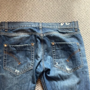 Blå italienska jeans med slitningar - Säljer ett par blå jeans med snygga slitningar och kontrastsömmar. Jeansen är tillverkade i Italien och har klassisk femficksdesign med raka ben. Materialet är jeans med en cool tvätt och detaljer på bakfickorna.