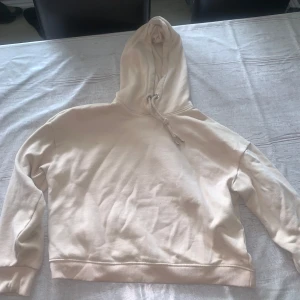 Vit/rosa hoodie med huva och snörning - Säljer en enkel och stilren vit/rosa hoodie med huva och snörning. Tröjan har långa ärmar och ribbade muddar vid ärmslut och nederkant. Perfekt för chill dagar eller när du vill ha en clean look.