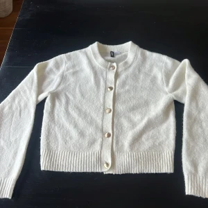 Vit kofta från H&M Divided med guldknappar - Superfin vit kofta från H&M Divided i storlek S. Koftan är stickad och har snygga guldiga knappar framtill, ribbade muddar och rund halsringning.