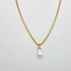 Guldhalsband och örhängen med pärldroppar - Snyggt set med halsband och örhängen i guldton med droppformade vita pärlor. Kedjan är klassisk och örhängena har små ringar med hängande pärldroppar, dekorerade med en liten guldfärgad detalj upptill. Perfekt för dig som gillar stilrena och eleganta smycken.