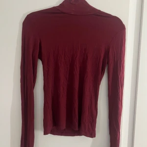 Vinröd polotröja från Gina Tricot - Säljer en vinröd polotröja från Gina Tricot i storlek S. Tröjan har lång ärm och en klassisk polokrage, perfekt för lager-på-lager. Materialet är mjukt och stretchigt, vilket gör den skön att bära. Enkel och stilren design som funkar till många olika outfits.