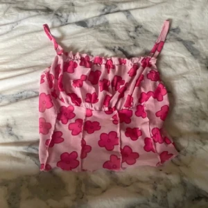 Rosa blommig linnetopp från Shein - Supersöt rosa linnetopp från Shein med starkt rosa blommönster. Tunt mesh-liknande material, smala axelband och croppad passform. Perfekt för dig som gillar färg och vill sticka ut med en lekfull vibe. Säljes i storlek XS.
