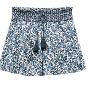 Superfin kjol från Zara - Supersöt kjol från Zara i vitt och blått med blommigt mönster och inbyggda shorts. De har bred smock i midjan, snörning med tofsar och är gjorda i mjuk bomull. Perfekta för varma sommardagar när du vill ha en chill och snygg look.