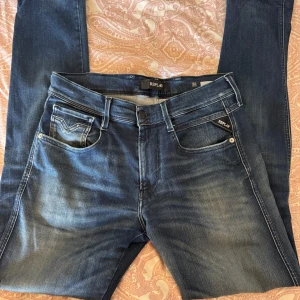 Replay Anbass jeans blå herr 32 - Snygga Replay Anbass jeans i klassisk blå tvätt med lätt slitning och raka ben. Jeansen har fem fickor, tydliga sömmar och logga på bakfickan. Skön passform och tillverkade i mjukt bomullsjeansmaterial. Nypris 1699kr så därav ett högre pris🛍️🛍️