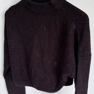 Svart stickad tröja med hög krage - Mysig svart stickad tröja med hög ribbad krage och långa ärmar. Tröjan har en loose passform och grovstickad struktur som ger en chill och avslappnad vibe. Perfekt att slänga på sig när det är lite kyligt ute. Liten i storleken