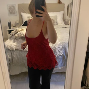 Röd spetsig linnetopp med tunna band - Snygg röd linnetopp med spetsdetaljer och tunna axelband. Toppen har en djup urringning fram och öppen rygg, samt vågig spetskant nertill. Storlek L men sitter fortfarande fint även om man är en mindre storlek.