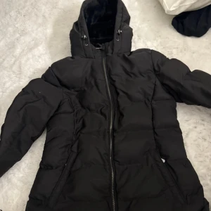 Svart pufferjacka från Zara med huva - Säljer en svart pufferjacka från Zara med mysigt foder i huvan. Jackan har dragkedja framtill, långa ärmar och två fickor på sidorna. 