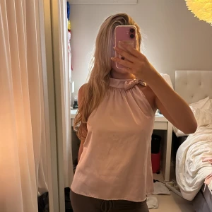 Ljusrosa halterneck blus med rosett - Supersöt ljusrosa blus i halterneck-modell med hög krage och en fin rosettdetalj vid halsen. Knappt använd, därav fint skick. Storlek S/M