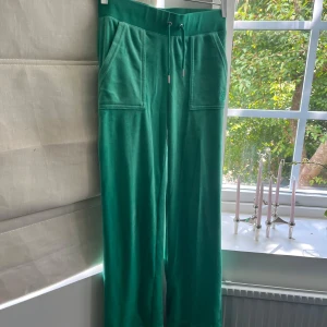 Gröna mjukisbyxor juicy couture - Snygga gröna mjukisbyxor i mjukt material med bred resår och snörning i midjan. Byxorna har stora fickor fram och bakfickor med lock och knappar. Modellen är rak och avslappnad, perfekt för chill dagar. Från Juicy Couture och insydda längst ner för att passa mig som ca 165 men de går att ta ur lätt